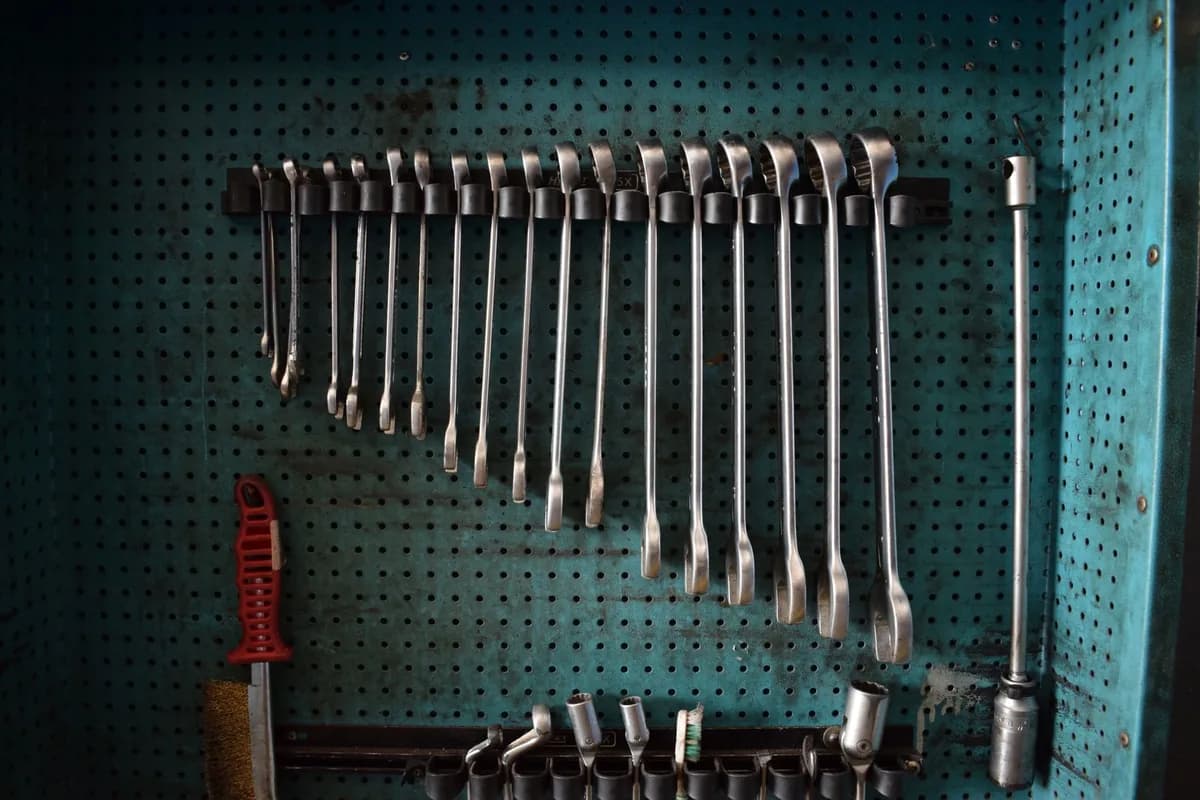 A row of combination wrenches hanging in size order on a worn teal pegboard above a rack of sockets