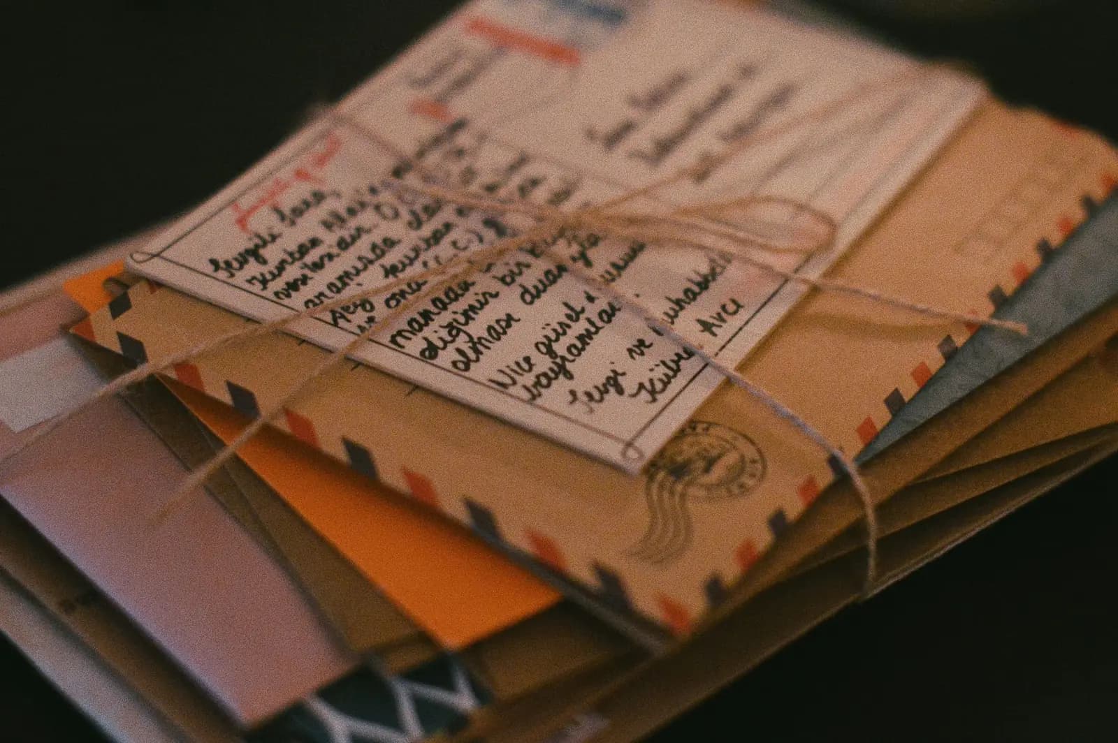A stack of airmail envelopes and a handwritten card tied together with twine on a dark table