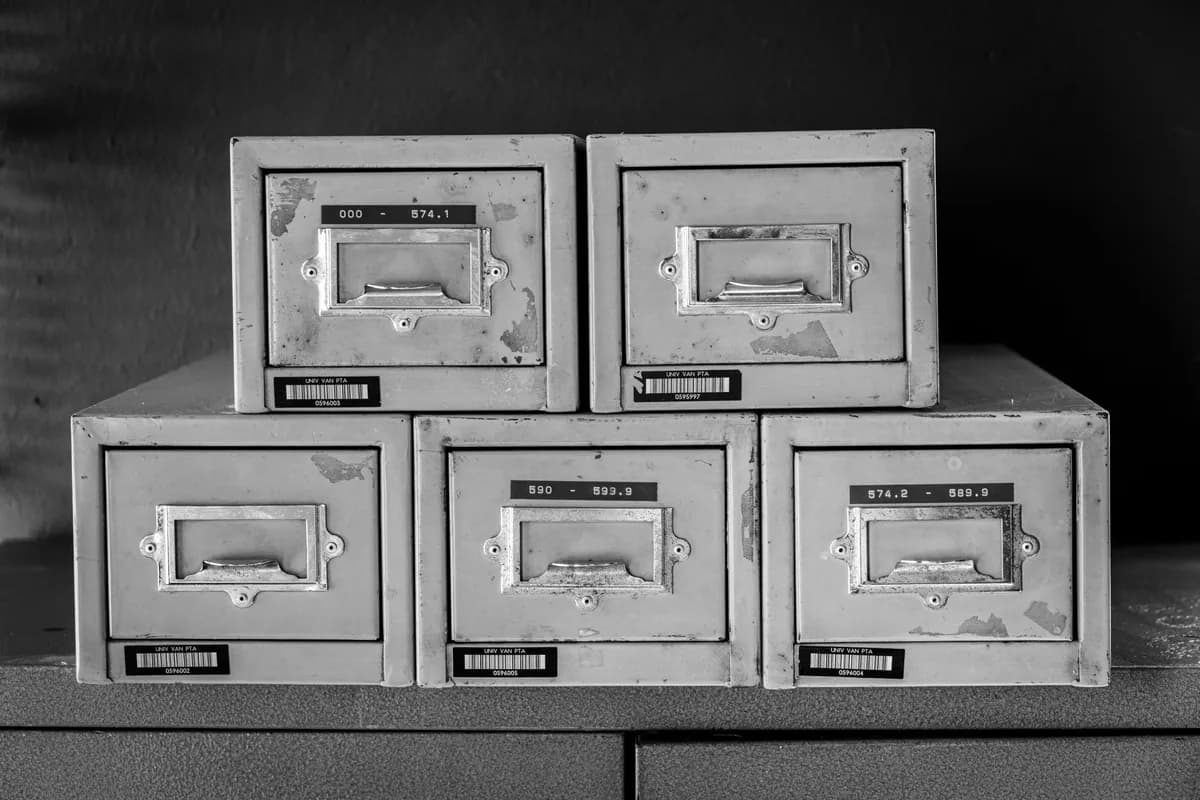 Five worn metal card-catalog drawers stacked on a shelf, photographed in black and white