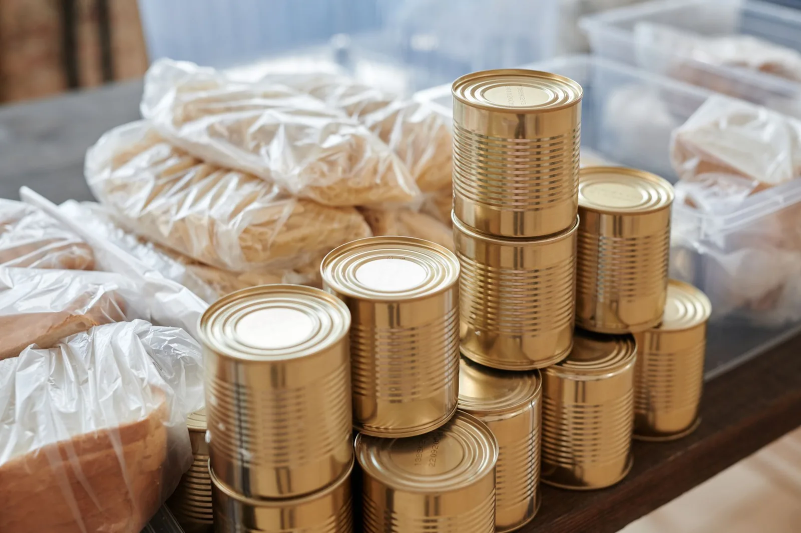Stacks of unlabeled food cans beside bags of bread on a table at a donation drive
