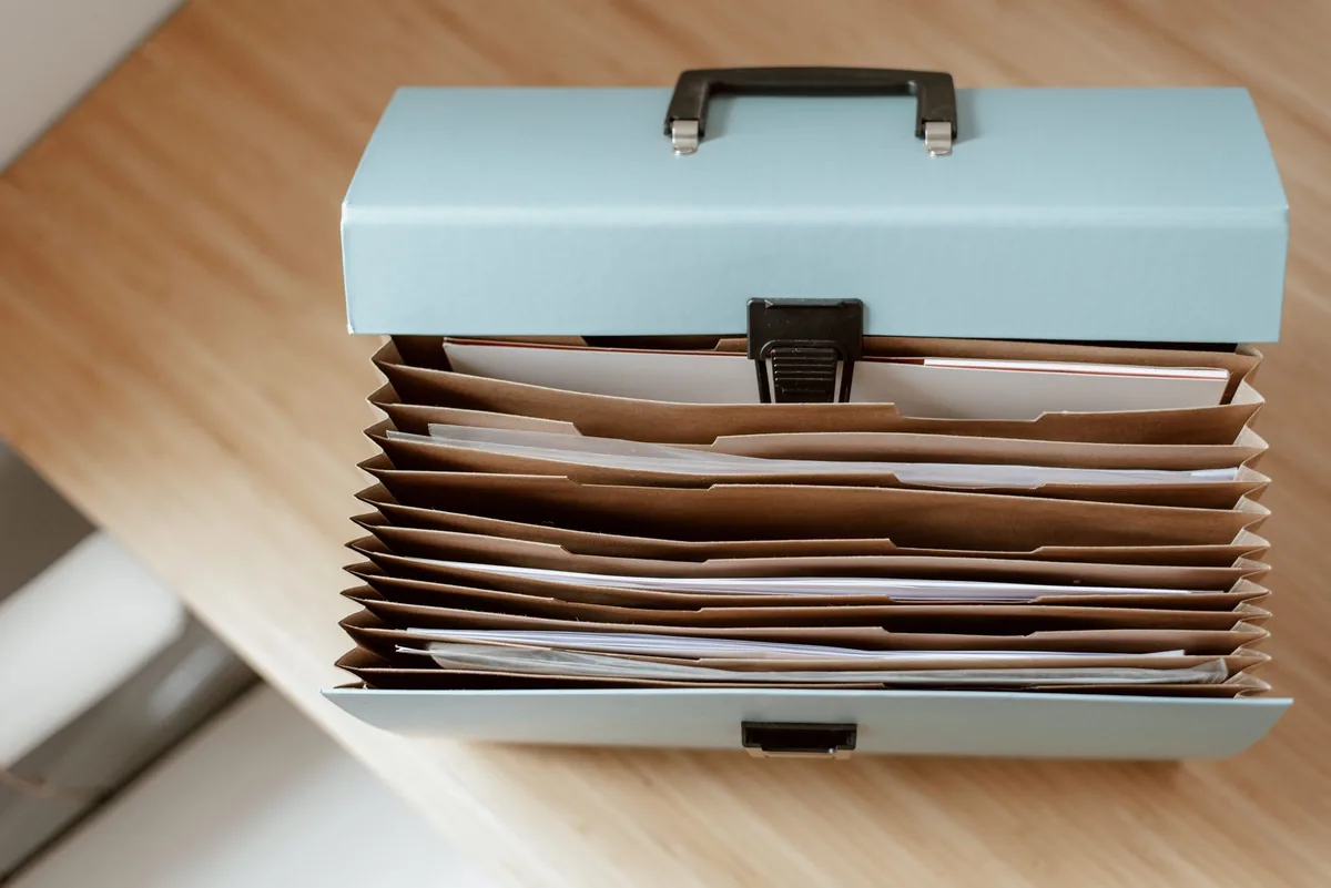 An overhead view of an open briefcase with documents and papers arranged neatly inside, on a wooden table