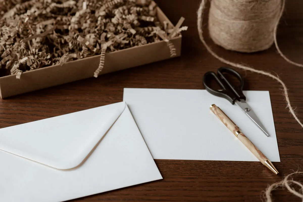 An overhead composition of a plain envelope and a pen resting on a desk, near a roll of twine and a pair of scissors